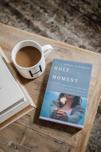 Copy of book, Holy in the Moment, is on a table alongside a cup of coffee.