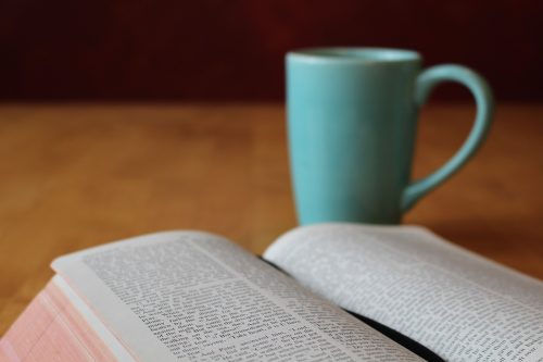 Open bible on table with a blue mug illustrates post on reading God's word for spiritual health.