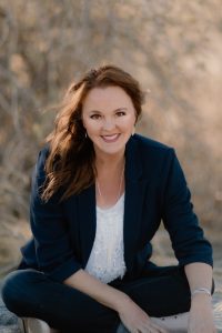 Author Lori Schumaker in front of tree background wearing a blue blazer.